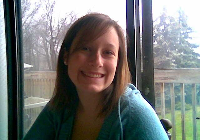 A woman smiling for the camera in front of a window.