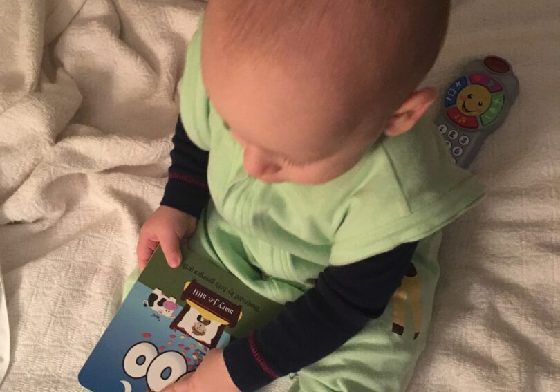 A baby is holding an electronic book on the bed.